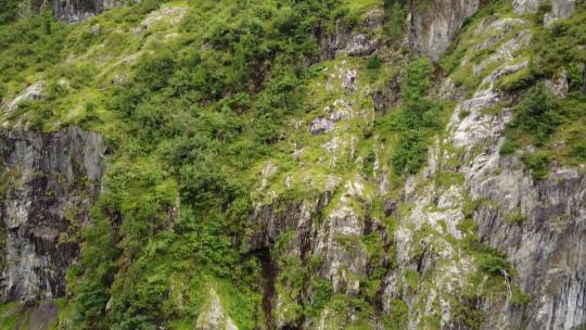 一架无人机在瑞士阿尔卑斯山的绿色岩石立面旁边飞行。空中拍摄