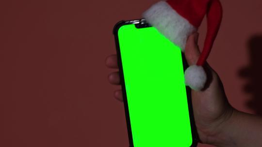 戴着圣诞老人红白帽子的手机，红色背景下带有色度键屏幕