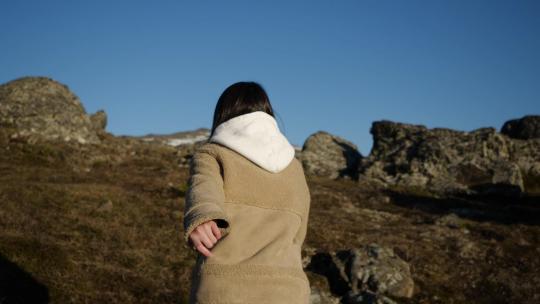 一个穿着米色夹克和连帽夹克的女孩在高山上奔跑