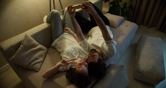 使用宝丽来相机在沙发上自拍的快乐美丽的年轻夫妇