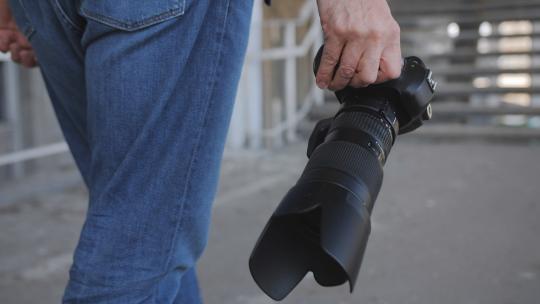 一名摄影记者手中拿着一台带有长焦镜头的相机的特写镜头