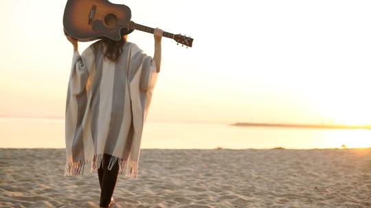 1985_一个女人拿着吉他走在日落的海滩上