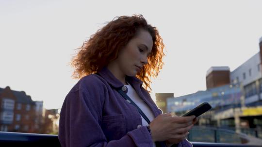 日落时分，年轻女子在城市里使用智能手机