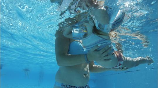 水下拍摄的无法辨认的女人教女儿在游泳池游泳