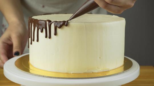 厨师挤压奶油。蛋糕上的巧克力糖衣。覆盖着巧克力和奶油的白色蛋糕。巧克力蛋糕装饰。乡村蛋糕。糕点。糕点厨师。现代蛋糕。