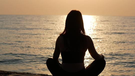 一名瑜伽女子坐在海看日落