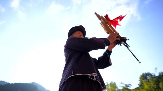 逆光下苗族少年吹起芦笙