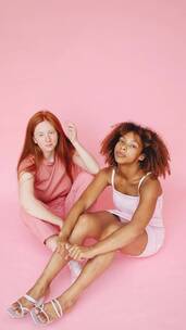 两个女人坐在粉红色的背景下看相机竖屏