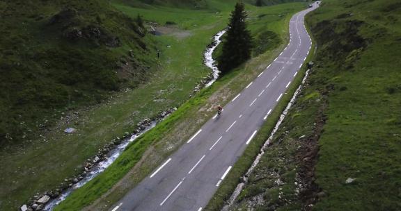 无人驾驶飞机空中平移图，一名骑自行车的人在法国比利牛斯山脉的一条平静的道路上爬上
