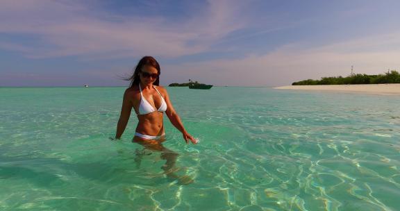 夏天白色沙滩和蓝色背景下海滩上阳光下度假的年轻美女模特4K高清在线视频素材下载