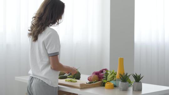 技能女孩站在家里厨房的桌子旁用刀切黄瓜