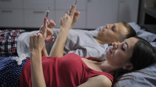 男女晚上躺在床上使用手机的特写侧视图。交流的新时代，夫妻沉迷于在线交流，沉迷于技术和过度使用。