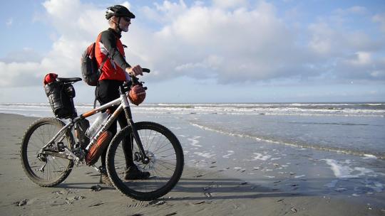 男人扶着自行车站在海边