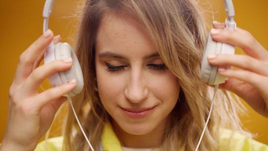 年轻女子在黄色背景下用耳机听音乐