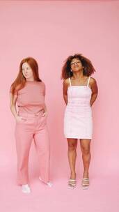 竖屏两名女子站在粉色背景下看相机