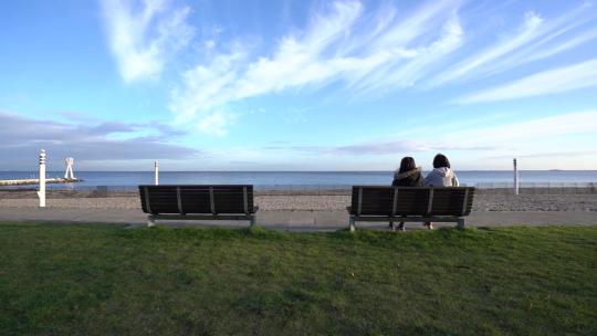 女孩坐在长凳上看着海滩的风景视频素材模板下载