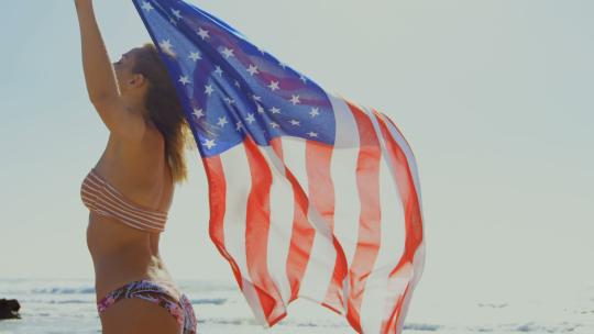 女人在海滩上举着美国国旗视频素材模板下载