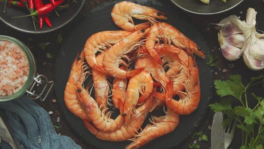 生鲜虾与各种配料，如柠檬新鲜香草、大蒜、辣椒放在黑石上菜盘上。俯视图，平铺。