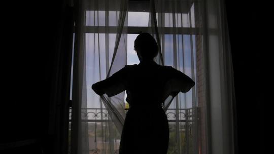 一个女人打开阳台的窗户，享受婚礼前的早晨