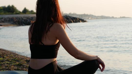 一名瑜伽女子坐在海边的莲花位置，看着太阳黎明的大海。
