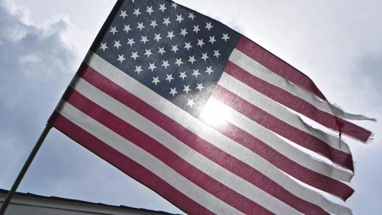 一面破烂的美国国旗在风中慢动作飘扬。