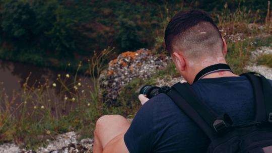 男摄影师在山崖边拍摄湖面