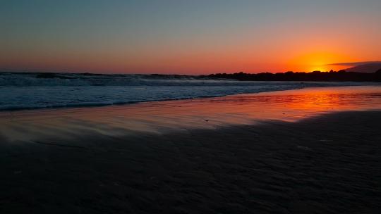 日落时海滩的低手推车照片，阳光美丽地反射在沙滩和海浪上com