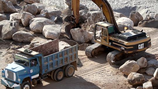 挖掘起重机将一块石头抬上卡车