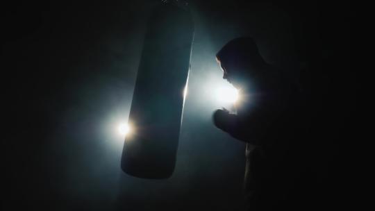 拳击手在昏暗的健身房打拳击沙袋