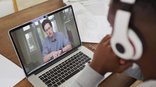 非裔美国男大学生戴着耳机在家里的笔记本电脑上进行视频通话视频素材模板下载