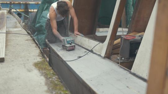 青年打磨木船甲板木板。