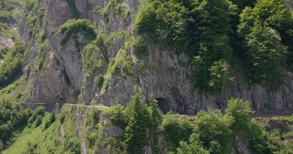 无人驾驶飞机在史诗般的岩石隧道周围平移，而四名骑自行车的人在自行车旅行通行证上投掷