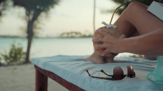 美女在海边躺椅上休息度假喝椰子水