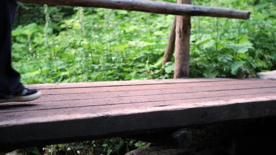 一个穿着深色宽裤子的女孩在树林里的木桥上慢动作过河视频素材模板下载
