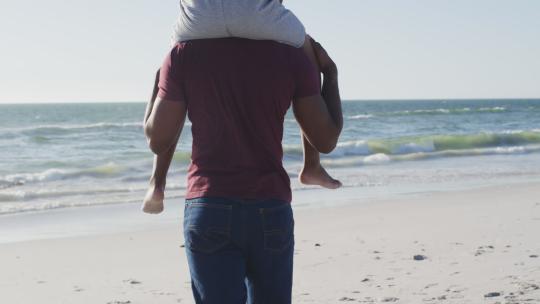 儿子坐在父亲肩上在海滩上散步