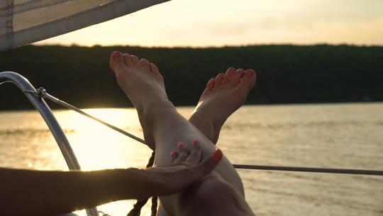 日落时，女性手触摸伴侣在帆船上放松的腿。度假的年轻人。lgbt夫妇在暑假