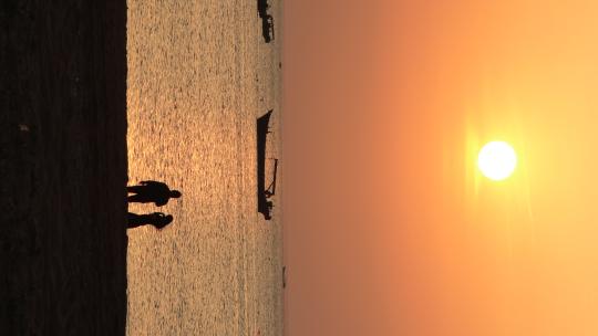 威海西海岸沙滩上游玩拍照的情侣落日剪影