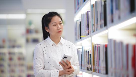 中年女性拿着手机在图书馆挑书