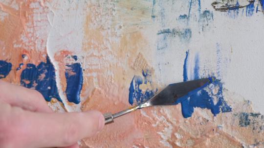 天才艺术家的手用铲子在画布上画一幅抽象画