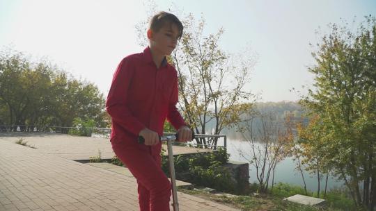 穿红色衣服的男孩在公园里骑踏板车。这个孩子积极地在户外度过时光。慢动作。