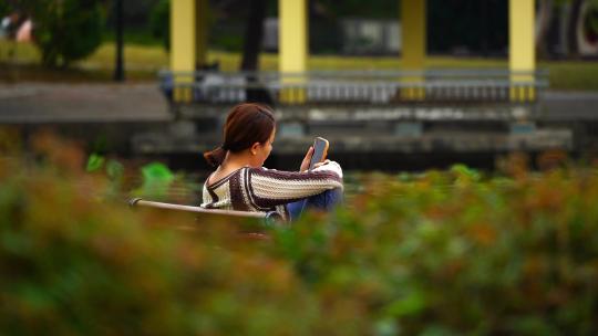 悠闲的女游客坐在长椅上看手机