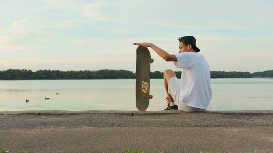 一个年轻人坐在河边用手转滑板