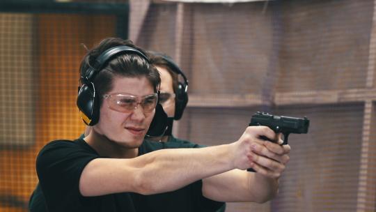 射击画廊。一个戴着防护眼镜和耳机的集中注意力的年轻人瞄准目标并射击