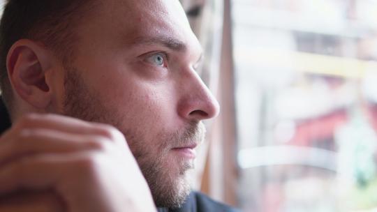 年轻英俊的男人独自坐在咖啡馆里，等待着，看着窗外。手放在面前。特写，4K