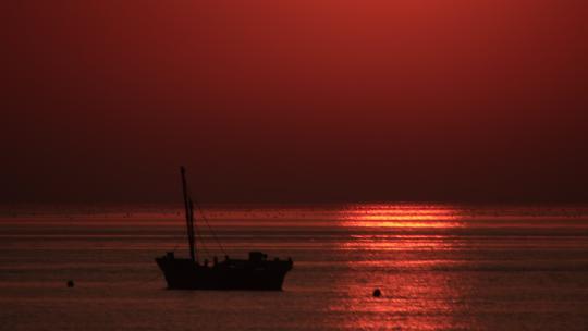 夕阳落日金色海面上的一条渔船