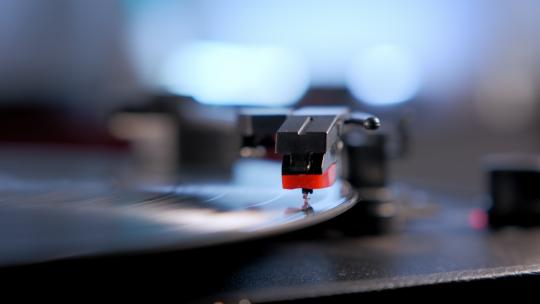 手将老式转盘放在旋转的乙烯基唱片上的特写镜头。
