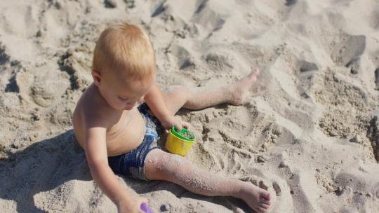 坐在沙滩上玩耍的小男孩