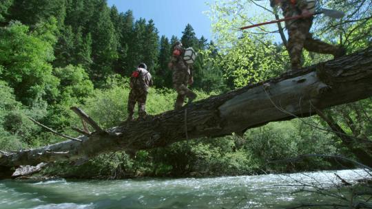 林场护林员背着工具走过湍急的河流进山巡护