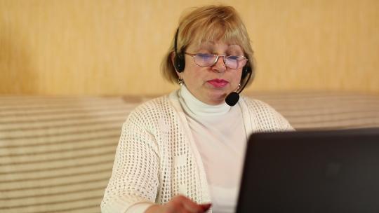 戴着耳机和麦克风的女人通过笔记本电脑与顾客交谈。女人通过笔记本电脑交流
