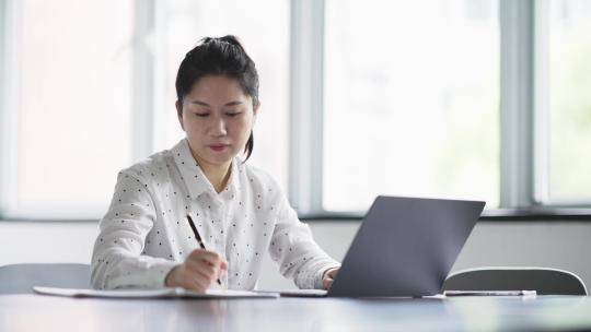 职业女性在电脑上工作，用笔记录